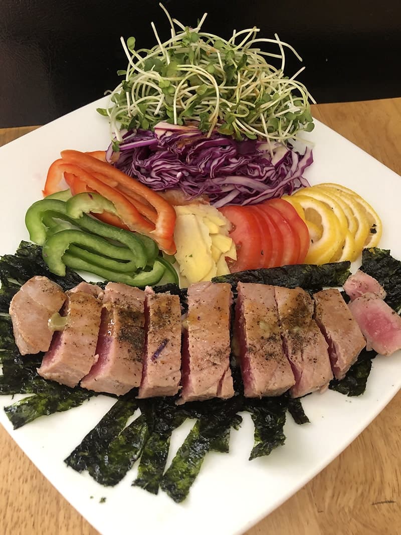 A colorful plate of sliced vegetables, greens and seared tuna